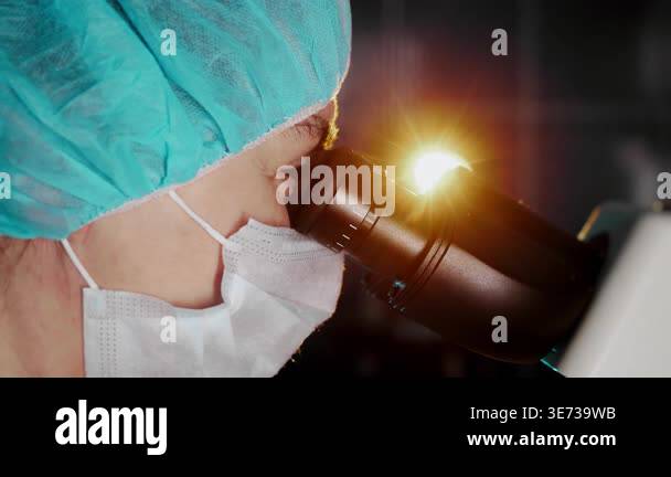 Close up of scientist in protective mask using microscope in laboratory ...