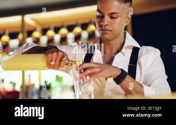 Concentrated barman carefully pouring yellow liquor from a bottle into ...