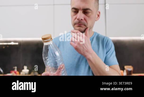 Thoughtful man studies plastic bottle touching cap before recycling ...