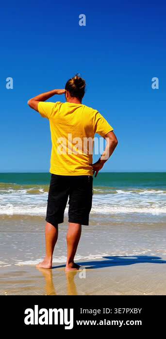 Man in yellow shirt standing on beach, saluting while looking at the ...