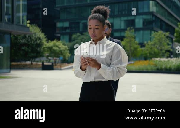 African American business woman walking in city using mobile phone ...