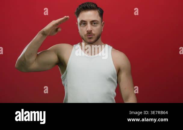 Young man with beard saluting with serious expression against red ...