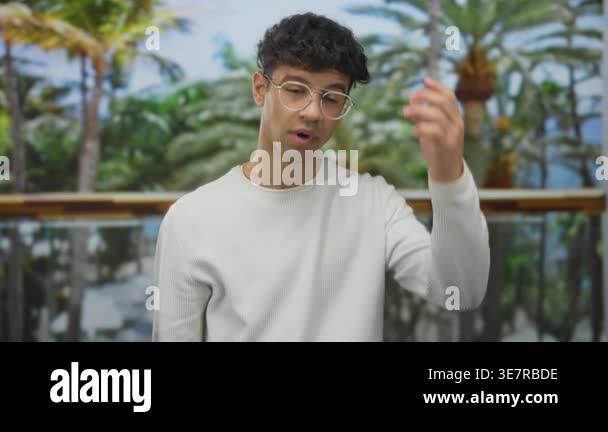 Man with curly hair and glasses in cream sweater touches forehead at ...