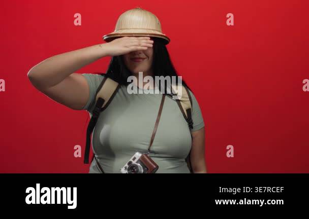 Woman saluting with pith helmet and camera around her neck over vibrant ...