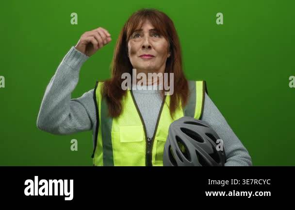 Senior hispanic woman standing against a green wall wearing a safety ...