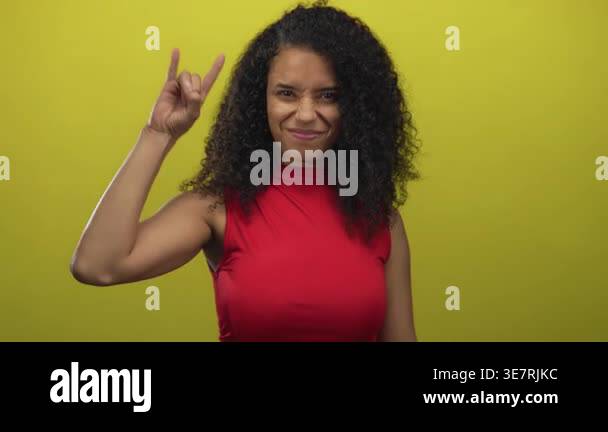 Woman in red dress making rock sign over yellow background, smiling ...