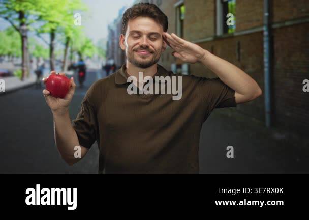 Young hispanic man holding shiny red apple in left hand and saluting ...