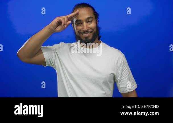 Man in white t shirt saluting with right hand to forehead, smiling and ...