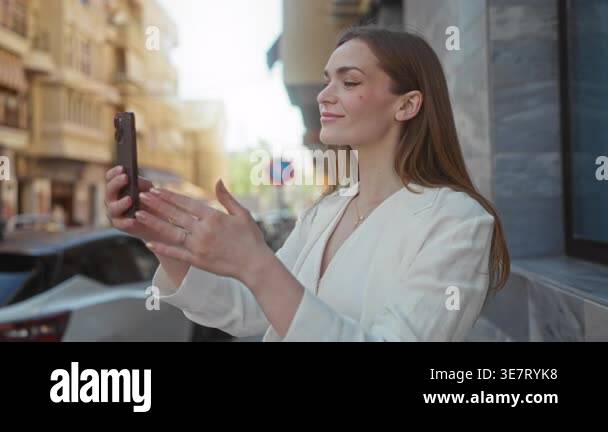 Young caucasian woman holding smartphone taking selfie on urban street ...