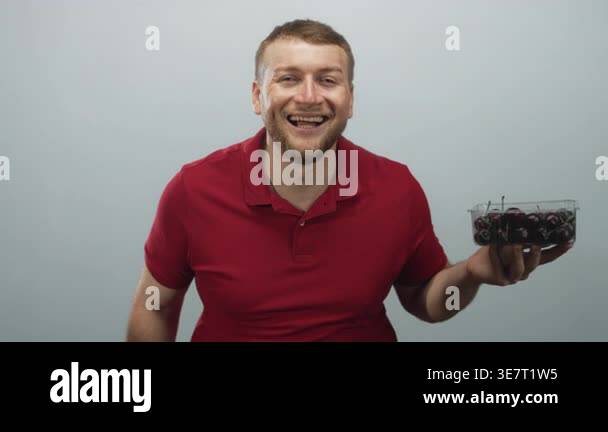 Man smiling and holding plastic container of cherries in studio with ...