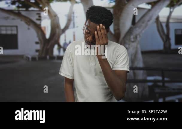 Man in white polo shirt and glasses touches forehead in front of ...
