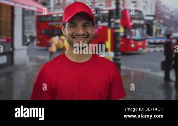 Young courier man in red cap smiling with visible face by red bus on ...