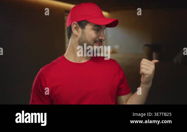 Man wearing red cap and t shirt points thumb to the side in an empty ...