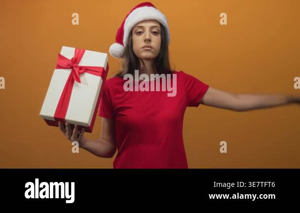 Woman holding white gift box with red ribbon and saluting in orange ...