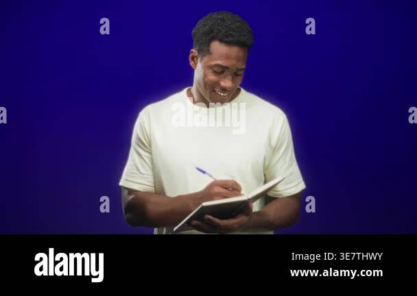 Man writing in notebook, pen in right hand, smiling and looking down at ...