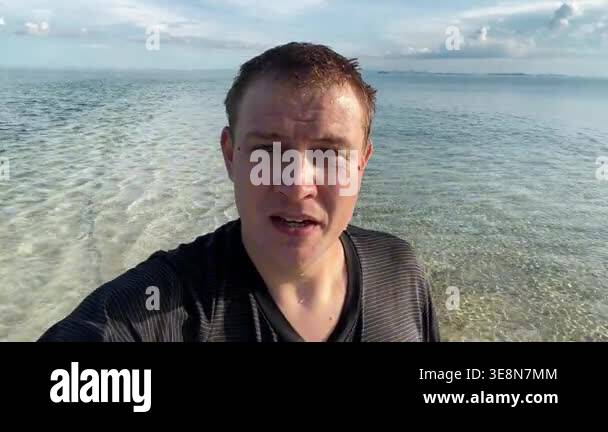 Wet male vlogger walking in shallow crystal clear tropical ocean water ...