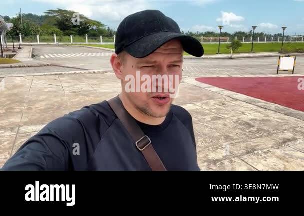 Male travel blogger in black cap and t-shirt talking to camera during ...