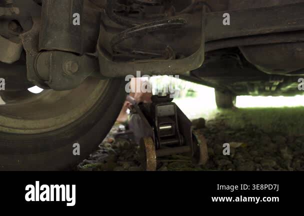 Low-angle close-up of a car being lifted with a hydraulic jack under ...