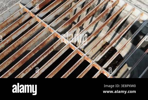 Rusty metal grate over a drainage channel, top view with sunlight and ...