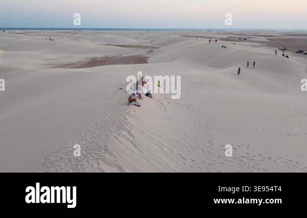 Wide view of desert sand dunes at sunset with groups of people seated ...