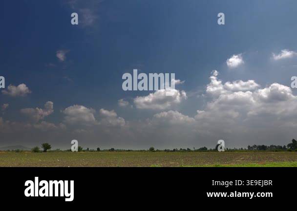Time lapse video of partly cloudy blue sky over flat plain farmland and ...