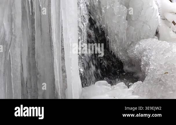 Many crowded icicles cover a natural frozen waterfall in cold air in ...