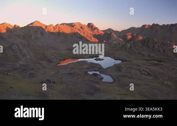 Morning sun rays illuminate high altitude mountain lakes beside rugged ...
