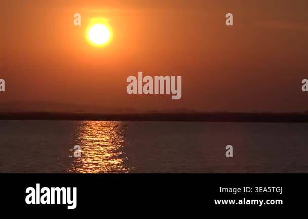 Time lapse of sunset with red orange hues reflecting across calm lake ...
