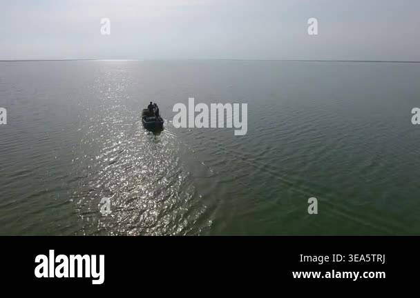 Aerial view of two fishermen sailing old wooden boat across calm lake ...