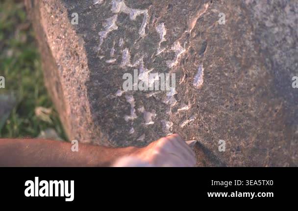 Hands carving marks into rock beside ancient petroglyph imagery and ...