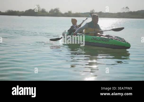 white man and child kayaking on lake, green inflatable kayak gliding ...