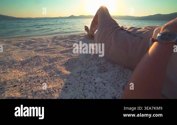 Woman relaxes and walks along white sand beach at sunset beside calm ...