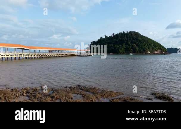 Long pier stretches across calm waters. Distant island rises green and ...