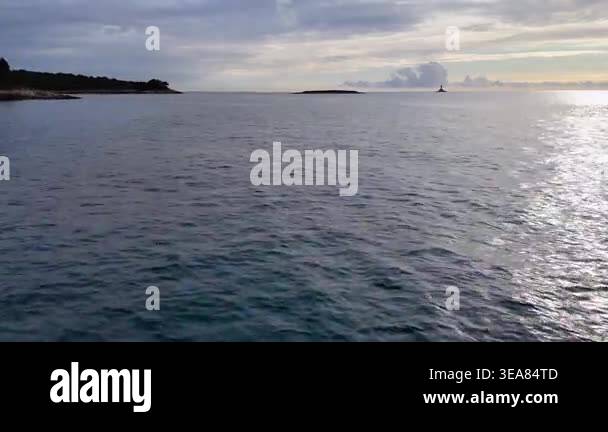 Calm sea water rippling under a cloudy sky with a distant island and a ...