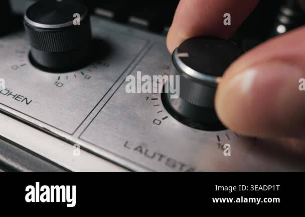 Fingers turn the black volume dial on a brushed metal audio amplifier ...