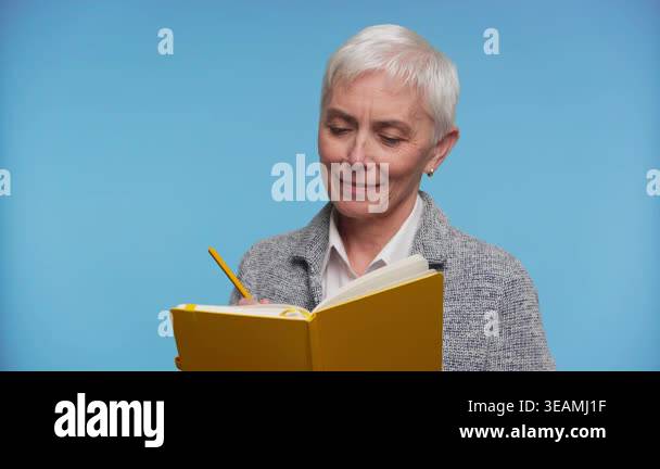 Portrait of an older woman smiling while writing in a yellow notebook ...