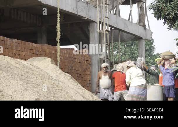 Three laborers carrying bricks at a construction site with a building ...