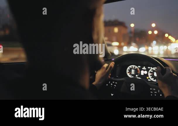 Backseat view on man driving car through bustling city at dusk under ...