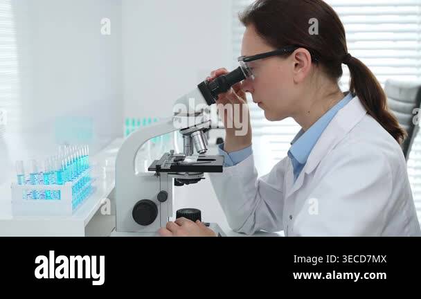 Female scientist in a lab coat and protective glasses examining test ...