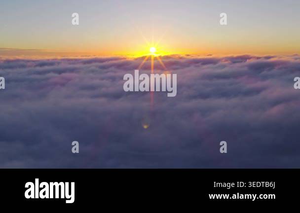 Aerial flight above glowing clouds at sunset with golden sunlight ...