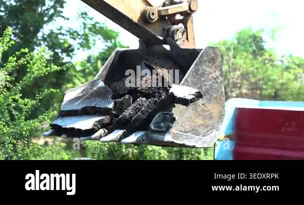 Excavator bucket loading broken asphalt and concrete into a dump truck ...