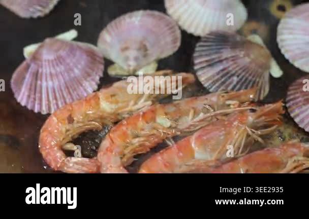 Assorted fresh seafood, including prawns, scallops, and clams, sizzling ...