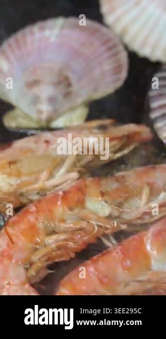 Assorted fresh seafood, including prawns, scallops, and clams, sizzling ...