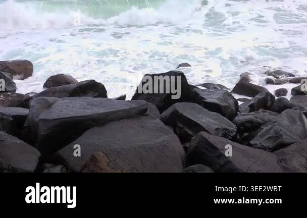 Serene coastal scene with dark volcanic rocks and turquoise waves ...