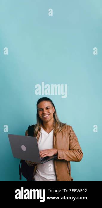 Happy young man with long hair and a backpack smiling while typing on a ...