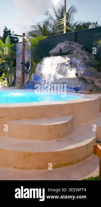 Sunny resort hotel swimming pool with an artificial waterfall flowing ...