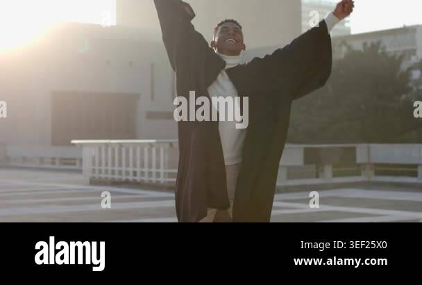 Pullback urging African American male graduate on rooftop tossing cap ...