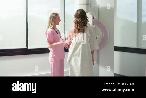 Female technician placing hand guiding patient in exam gown at ...