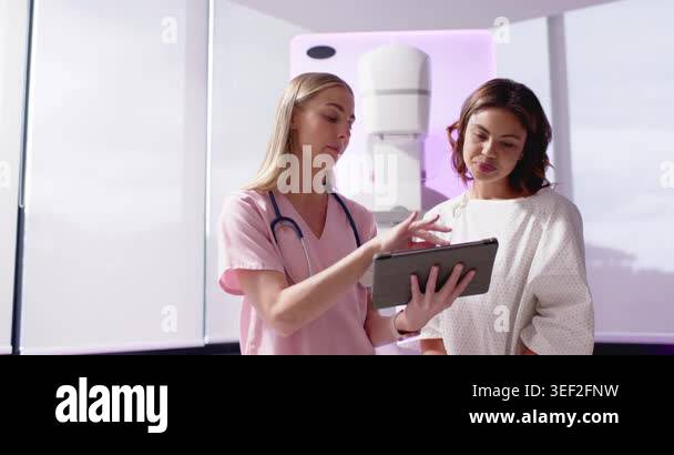 Female clinician and female patient in mammography room tapping tablet ...
