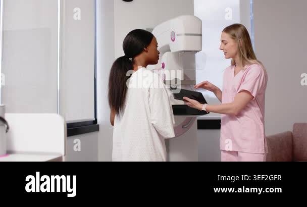 Diverse patient placing hand on mammogram; pink-scrub tech gesturing ...